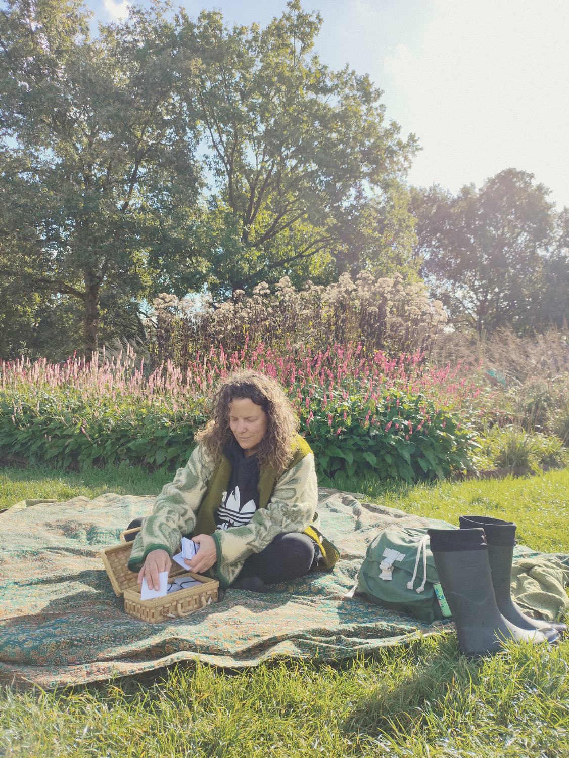 Anneke op een kleed in het gras met een mand kaarten